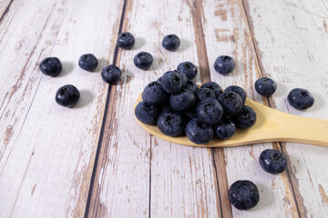 Freshly picked blueberries in wooden bowl. Juicy and fresh blueberries with green leaves on rustic table.