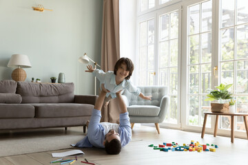 Strong young father holding happy cheerful little son. Kid playing airplane with open flying arms,...