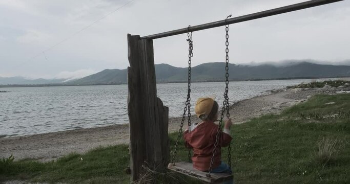 Capture a delightful moment as a boy enjoys a swing against the picturesque backdrop of Lake Sevan, surrounded by stunning natural beauty.