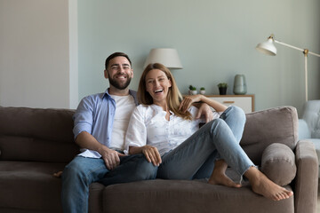 Cheerful attractive young couple relaxing on soft couch together, hugging, smiling, laughing,...