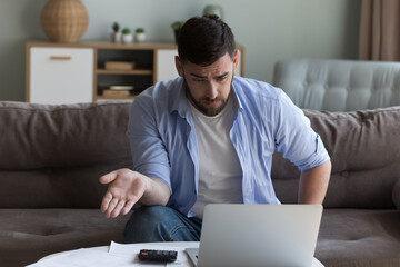Shocked stressed millennial customer man annoyed about online application wrong work, using laptop,...