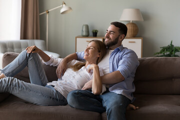Cheerful dreamy couple in love enjoying leisure time, relaxing at cozy home, lying on sofa,...