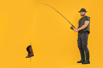 Fisherman with fishing rod and old boot on yellow background, space for text