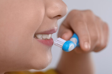 Girl brushing her teeth with toothbrush on light grey background, closeup