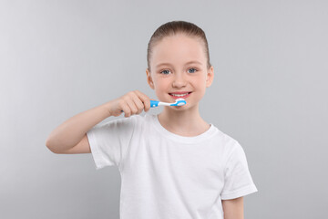 Happy girl brushing her teeth with toothbrush on light grey background