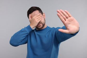 Embarrassed man covering face on light grey background