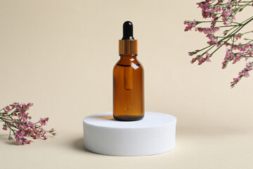 Bottle of cosmetic oil and flowers on beige background