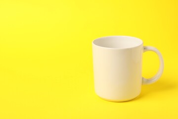 One white ceramic mug on yellow background, space for text
