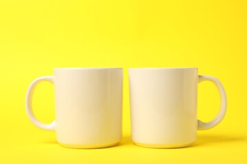 Two white ceramic mugs on yellow background