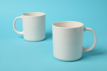 Two white ceramic mugs on light blue background