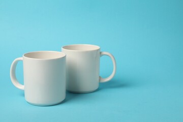 Two white ceramic mugs on light blue background, space for text