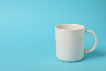 One white ceramic mug on light blue background, space for text