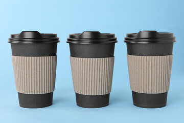 Paper cups with black lids on light blue background. Coffee to go