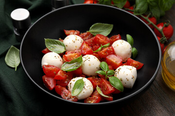 Tasty salad Caprese with tomatoes, mozzarella balls and basil on wooden table, closeup