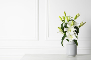 Beautiful bouquet of lily flowers in vase on light table near white wall, space for text