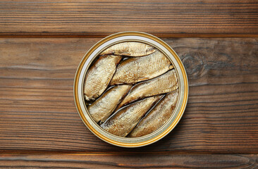 Open tin can of sprats on wooden table, top view