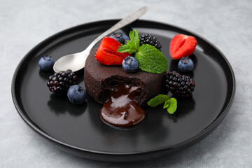 Plate with delicious chocolate fondant, berries and mint on grey table, closeup