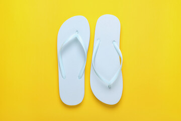 Stylish white flip flops on yellow background, top view