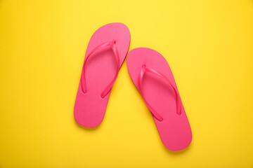 Stylish pink flip flops on yellow background, top view