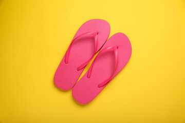 Stylish pink flip flops on yellow background, top view