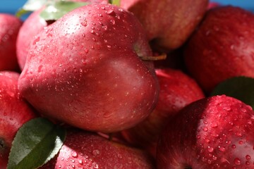 Ripe red apples with water drops and green leaves as background, closeup