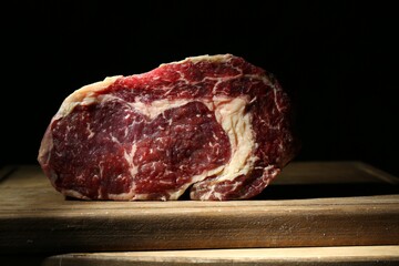 Piece of raw beef meat on wooden board against black background, closeup
