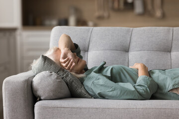 Calm senior sleepy woman napping at home, lying on back on sofa with closed eyes, sleeping on...