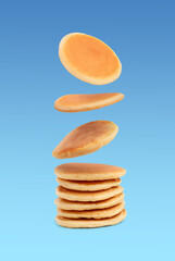 Many tasty fresh pancakes falling on light blue background