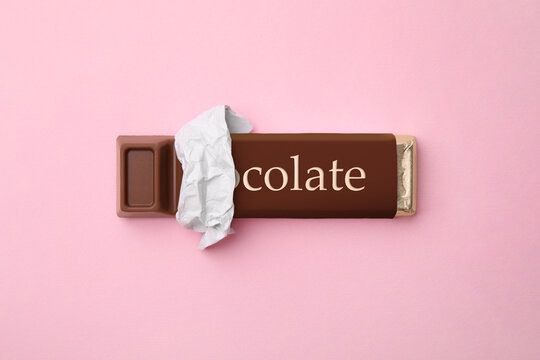 One chocolate bar in packaging on pink background, top view