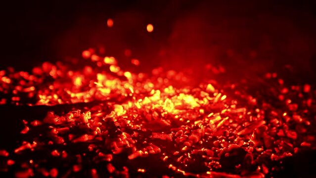 Blowing air on the burned charcoal. The pieces of burnt wood start to glow red and smoke goes up. Close up.