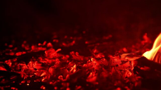 Glowing pieces of charcoal sparkling beautifully. Little flames of fire break out again. Close up.