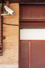 Surveillance camera hanging on the wall of a building with clay brick walls and metal portals...