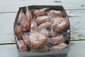 Pile of donuts wrapped in plastic in a cardboard box on a table 