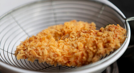 Fried chicken in a sieve on the stove. Selective focus.
