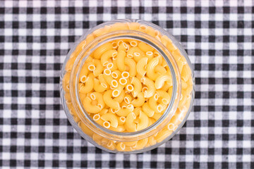 Uncooked Chifferi Rigati Pasta in Glass Jar on Black Checkered Towel. Fat and Unhealthy Food. Scattered Classic Dry Macaroni. Italian Culture and Cuisine. Raw Pasta