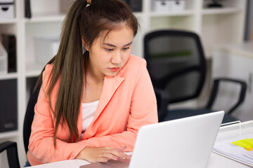 Beautiful young Asian woman in casual clothing using laptop computer while working at home office. research, studying literature.