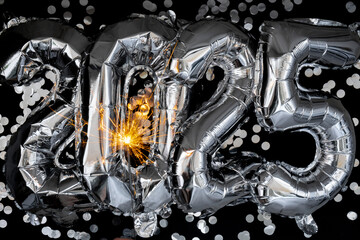 Happy new year 2025 metallic balloons with confetti and sparkler firework Bengal lights on dark black background. Greeting card silver foil balloons numbers Christmas holiday concept. Celebration