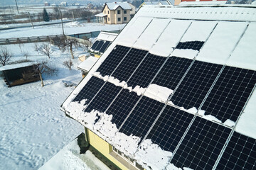 Aerial view of snow melting from covered solar photovoltaic panels installed on house rooftop for...