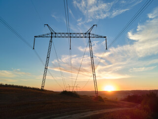 Dark silhouette of high voltage tower with electric power lines at sunrise. Transmission of electric energy concept