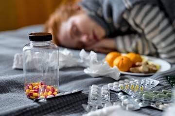 died ginger girl lying on bed, different drugs, pills in the foreground of photo. red-haired girl shocked and unconsciousness because of overdose. concept pharmacist and drug. blurred background