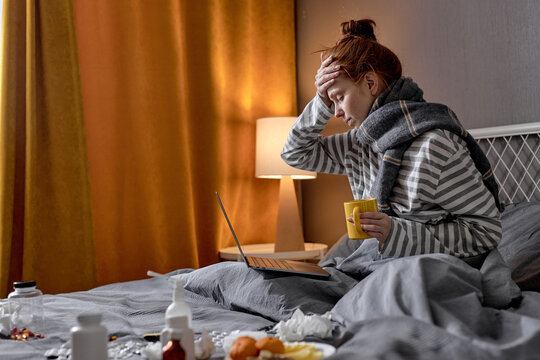 redhead woman having cough, sneezing, feeling sick while working online from home, freelance during covid-19, coronavirus, omicron. female with headache drinking hot tea to lower the temperature