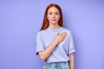 redhead girl putting her arm on her breast, you are welcome. closeup portrait, red-haired girl with palm on her hear looking at camera isolated blue background girl saying the word love