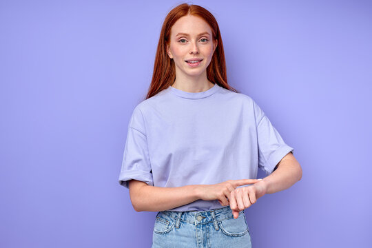 attractive smiling ginger girl asking time, touching her arm, wrist, what time is it now close up portrait isolated blue background it is time