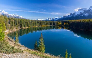 Fototapeta na wymiar Treelined Shore Blue Rocky Mountain Lake, Scenic Autumn Landscape, Distant Snow Covered Peaks, Banff National Park, Canadian Rockies Alberta Foothills