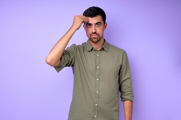 Young serious bearded deaf mute man with hand on his forehead showing the word clever, using sign language on blue background isolated close up portrait