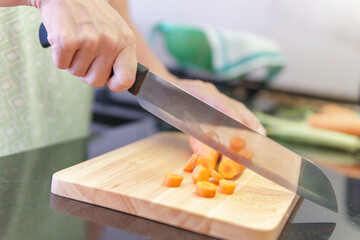 Woman hands cutting fresh orange carrots in a kitchen