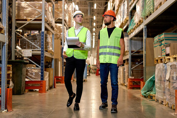 Obraz premium Caucasian engineers in helmets and uniform, team checking goods and supplies on shelves in warehouse. logistic and business export. good management system to support working with industrial business.