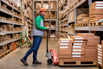Skilled warehouse employee pushing manual pallet jack and working in factory storage room, warehouse worker transporting cardboard goods delivery. logistics and distribution concept