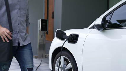 A man unplugs the electric vehicle's charger at his residence. Concept of the use of electric...