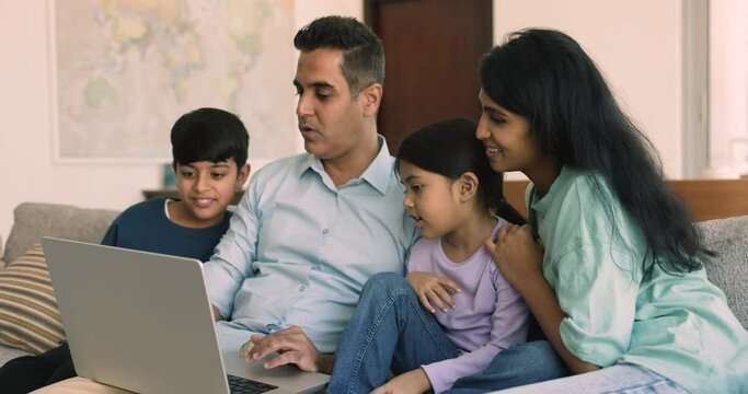 Indian family with kids make purchase online sit on sofa use laptop, choose goods, discuss internet shopping, enjoy easy and comfortable electronic commerce. E-commerce, retail services, modern tech